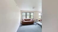 Located at 109 Dryden Rd in Ithaca, NY, this 4-bedroom, 2-bathroom unit offers a well-organized single-floor layout designed to comfortably accommodate multiple residents. The living room is bright and welcoming, featuring large black-framed windows that frame views of surrounding greenery, soft carpeted flooring, and a wall-mounted AC unit. It flows naturally into a dedicated dining area, also carpeted and lit by a generous window overlooking the neighborhood. The kitchen is efficiently laid out with white cabinetry accented by warm wood trim, light tile flooring, a double sink, dishwasher, and ample counter and storage space. Each of the four bedrooms is modestly sized with carpeted floors, natural light from windows with blinds, and individual wall AC or baseboard heating units. The primary bedroom offers slightly more space with room for a dresser and seating. Both bathrooms share a consistent design featuring light tile flooring, a vanity with storage, a toilet, and a tub-shower combination with a sliding glass door. Three hallways connect the rooms efficiently throughout the unit, contributing to a functional and straightforward floor plan suited for shared living in the heart of Ithaca.