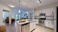 This single-floor residence offers a thoughtfully designed layout encompassing two bedrooms, two bathrooms, a utility room, and two closets connected by a central hallway. The open-concept kitchen and living area forms the heart of the home, where a central island with granite countertops and a stainless steel undermount sink serves as a functional focal point. Pendant lighting illuminates the island, complementing the stainless steel appliances, including a range, over-the-range microwave, and dishwasher. Light-toned cabinetry with sleek hardware lines the kitchen walls, providing ample storage.

The living area flows naturally from the kitchen and features wood-style flooring, a ceiling fan, and French doors that invite natural light and outdoor views. Each bedroom includes wood-style flooring, a ceiling fan, and window treatments. The primary bedroom features its own closet and dedicated bathroom access. Both bathrooms are finished with granite-topped vanities, light wood cabinetry, large-format tile flooring, and a soaking tub. The walk-in closet includes wire shelving for organized storage throughout.