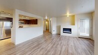 Located in King City, Oregon, this 2-bedroom, 2-bathroom single-floor residence offers a well-designed layout with a thoughtful mix of comfort and functionality. The open-concept living, dining, and kitchen area forms the heart of the home, featuring light wood-style flooring, a textured ceiling, and a sleek built-in electric fireplace that anchors the living space. Large windows allow abundant natural light to fill the room, providing views of the surrounding neighborhood. The kitchen is efficiently designed with rich dark-wood cabinetry, white countertops, stainless steel appliances including a refrigerator, range, and microwave, and track lighting overhead. A pass-through counter connects the kitchen to the living and dining area. Both bedrooms are carpeted and generously sized, with multiple windows offering ample natural light. The primary bedroom includes a walk-in closet with wire shelving. The bathrooms feature wood-toned vanity cabinetry, white countertops, and wood-style flooring. Additional highlights include four closets, a dedicated pantry, a laundry area, and a private balcony. The entrance hallway provides a clean transition into the main living spaces with consistent flooring throughout.