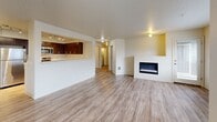 Located in King City, Oregon, this 2-bedroom, 2-bathroom single-floor residence offers a well-designed layout with a thoughtful mix of comfort and functionality. The open-concept living, dining, and kitchen area forms the heart of the home, featuring light wood-style flooring, a textured ceiling, and a sleek built-in electric fireplace that anchors the living space. Large windows allow abundant natural light to fill the room, providing views of the surrounding neighborhood. The kitchen is efficiently designed with rich dark-wood cabinetry, white countertops, stainless steel appliances including a refrigerator, range, and microwave, and track lighting overhead. A pass-through counter connects the kitchen to the living and dining area. Both bedrooms are carpeted and generously sized, with multiple windows offering ample natural light. The primary bedroom includes a walk-in closet with wire shelving. The bathrooms feature wood-toned vanity cabinetry, white countertops, and wood-style flooring. Additional highlights include four closets, a dedicated pantry, a laundry area, and a private balcony. The entrance hallway provides a clean transition into the main living spaces with consistent flooring throughout.