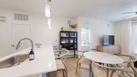 This well-appointed 1-bedroom, 1-bathroom residence offers a clean, modern aesthetic defined by bright white walls, light wood-style flooring, and an open, airy layout throughout. The combined kitchen and living area forms the heart of the home, where a galley-style kitchen impresses with white shaker cabinetry, stainless steel appliances including a range, microwave, and dishwasher, and a sleek white quartz island and countertops. Pendant lighting adds a refined touch overhead. The dining area flows naturally from the kitchen, creating a cohesive and functional open-concept living space. The living room benefits from large windows and a glass door that invite abundant natural light, complemented by neutral carpeting and a ceiling fan. The bedroom is a serene retreat, featuring multiple windows with sheer curtains, a ceiling fan, and generous natural light. It connects directly to a spacious walk-in closet with wire shelving and to the full bathroom, which offers a lengthy vanity with white cabinetry, a large mirror, and wood-look flooring. Throughout the residence, a consistent neutral palette and modern finishes create a cohesive, inviting atmosphere ideal for comfortable everyday living.