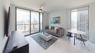 Located in the heart of Miami's vibrant Brickell district at 86 SW 8th Street, this contemporary high-rise residence offers a sleek, modern living experience defined by clean lines and abundant natural light. Floor-to-ceiling sliding glass doors and expansive windows frame dramatic panoramic views of the Miami skyline throughout the space, creating a seamless connection between interior and exterior.

The open-concept kitchen is outfitted with warm wood-grain cabinetry, crisp white quartz countertops, and a full suite of stainless steel appliances, including a French door refrigerator, range, and built-in microwave. Light porcelain tile flooring flows consistently throughout the residence. The living area is bright and airy, anchored by large glazed openings that flood the room with natural light and city views.

Multiple bedrooms provide generous accommodations, each featuring access to sweeping skyline vistas through floor-to-ceiling windows. The bathrooms are elegantly appointed with marble-surround walk-in showers, dual vanities topped with light stone countertops, pendant lighting, and large-format tile flooring. Built-in closets offer practical storage solutions. The overall aesthetic throughout is contemporary and refined, with a neutral palette that highlights the spectacular urban backdrop of downtown Miami.
