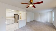This single-floor residence offers a clean, open layout designed for comfortable everyday living. The entryway welcomes residents through a paneled front door with a transom window, transitioning from marble-style tile flooring into the main living area. The living room is generously proportioned, featuring neutral-toned carpet, a ceiling fan with a light fixture, and a large sliding door covered by vertical blinds that allows natural light to filter into the space.

The kitchen is positioned adjacent to the living area and is accessible via an open pass-through. It is equipped with stainless steel appliances, including a gas range, over-the-range microwave, dishwasher, and refrigerator. White shaker-style cabinetry lines the walls, complemented by light quartz countertops and the same marble-style tile flooring as the entryway. A peninsula provides additional counter space and separates the kitchen from the adjoining areas.

The bedrooms are carpeted and bright, each featuring windows that bring in natural light and paneled closet doors offering ample storage. The overall palette throughout the residence is light and neutral, contributing to a clean, airy ambiance across all rooms.