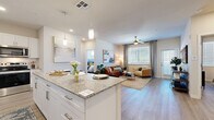 Located in Mesa, AZ, this well-appointed 1-bedroom, 2-bathroom residence offers a thoughtfully designed open-concept layout with modern finishes throughout. The kitchen serves as a central hub, featuring crisp white cabinetry, granite countertops, stainless steel appliances, a deep undermount sink, and a large island with pendant lighting and seating for three — ideal for both casual dining and entertaining. Wood-look plank flooring flows seamlessly into the open living room, which is bright and airy thanks to large windows with blinds, a ceiling fan, and access to an exterior door. The bedroom is a serene retreat, complete with a ceiling fan, natural light from a window with teal drapes, and direct access to a private en-suite bathroom. This primary bath features a granite-topped vanity with white cabinetry, a glass-enclosed walk-in shower, and wood-look flooring. A second full bathroom mirrors the same refined aesthetic, offering a soaking tub with shower, a granite vanity, and matching finishes. Two spacious walk-in closets provide generous storage, each fitted with multi-level hanging rods and wood-look flooring. The overall ambiance is clean, contemporary, and cohesive, with a neutral palette that lends itself to effortless personalization.