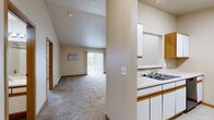 This one-bedroom, one-bathroom apartment in West Fargo, North Dakota offers a practical and comfortable single-floor layout. The open-concept kitchen and living area form the heart of the unit, with the kitchen featuring white cabinetry with wood-trimmed accents, white appliances including a dishwasher and refrigerator, a double sink, and light tile flooring. A pass-through window connects the kitchen to the living space, which is finished with plush carpet and highlighted by a sliding glass door that fills the room with natural light and provides access to an outdoor patio. The bedroom is a generously sized, carpeted retreat with a large window offering exterior views, baseboard heating, and direct access to a dedicated walk-in closet with wire shelving for organized storage. The full bathroom features tile flooring, a vanity with wooden trim, and a clean, neutral finish. A standout feature of this unit is the in-unit laundry area, equipped with washer and dryer hookups and additional wire shelving, adding everyday convenience. Throughout the unit, warm neutral tones, wood-trimmed doors, and consistent baseboard heating create a cohesive and functional living environment.