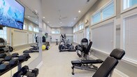Located at 6880 Rivers Ave in North Charleston, South Carolina, this well-appointed fitness center offers a comprehensive workout environment designed to meet a wide range of exercise needs. The single-floor facility features a bright, open layout with neutral gray walls, light-colored carpet flooring, and elevated ceilings that contribute to a spacious, airy atmosphere.

Natural light streams in abundantly through rows of large, white-trimmed windows with adjustable blinds lining the walls, while recessed ceiling lights and ceiling fans ensure consistent illumination and comfortable airflow throughout the space. Full-length mirrors are strategically placed to enhance the sense of openness and support proper form during workouts.

The cardio section is well-equipped with multiple Star Trac treadmills and elliptical trainers, as well as a stationary cycling bike, providing diverse options for cardiovascular exercise. The strength training area features a multi-function cable machine, TKO adjustable weight benches, and a full rack of dumbbells in varying weights, accommodating both beginner and advanced fitness routines.

Additional amenities include a wall-mounted flat-screen television, exercise mats, stability balls, and organizational storage for accessories. The overall design is clean, functional, and welcoming, making this fitness center a practical and well-maintained facility for residents in the North Charleston community.
