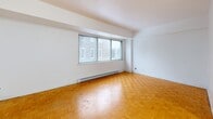 Located at 500 Avenue des Pins Ouest in the heart of Montréal, this efficiently designed studio unit offers a thoughtful layout that maximizes every square foot of its compact footprint. The main living area is immediately inviting, showcasing warm honey-toned parquet flooring laid in a classic checkerboard pattern that extends throughout the space, reflecting natural light and adding character to the clean, white-walled interior. A wide multi-pane window anchors the living area, offering views of the surrounding neighbourhood's brick architecture and allowing generous daylight to fill the room. A baseboard heating system runs along the exterior wall, ensuring comfort throughout the colder Montréal seasons. The open kitchen is neatly partitioned from the main living space, featuring white cabinetry, a full-size refrigerator, and tiled flooring that distinguishes it from the parquet areas. A dedicated entrance corridor leads into the unit and is flanked by two closets, providing practical and organized storage. The bathroom is fitted with white ceramic tile surrounding a full soaking tub with overhead shower, complemented by a vanity with storage and light tile flooring. The unit's crisp white palette throughout creates a bright, neutral canvas well-suited to urban living in this vibrant Montréal neighbourhood.