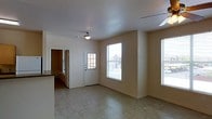 This single-story space offers a straightforward, functional layout with a clean and minimalist design. The main living area is an open room finished with light-toned tile flooring that runs throughout, contributing to a bright and cohesive feel. Neutral beige walls and a flat white ceiling with a central light fixture keep the space feeling simple and well-lit.

Natural light is a notable feature, with multiple windows along the exterior wall — including a tall vertical window and a partially visible window to the right — allowing generous daylight to fill the room and providing views of the surrounding neighborhood. A white paneled entry door with glass panes further contributes to the flow of natural light into the space.

To one side, a partial view into an adjacent area reveals what appears to be a kitchen, identifiable by a countertop edge and cabinetry. An interior doorway connects this area seamlessly to the main living space, supporting a practical open-concept feel.

Overall, the space presents a modest, move-in-ready environment with an emphasis on natural light, easy-to-maintain flooring, and a functional, no-frills layout suited for everyday living.