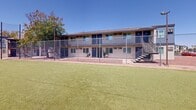 Located at 1950 North 43rd Avenue in Phoenix, Arizona, this single-level outdoor recreational facility serves as a central community hub within a residential complex. The centerpiece of the space is a generously sized artificial turf field, enclosed by a chain-link fence that defines the boundaries of the play area and provides a safe, contained environment for a variety of activities.

The turf surface is well-maintained and vibrant, offering a functional and visually appealing ground cover well-suited to the arid Phoenix climate. Surrounding the field, decomposed granite pathways and desert-landscaped borders frame the perimeter, reflecting a practical approach to outdoor design in the Southwest.

Flanking the turf area are two-story residential buildings featuring neutral stucco exteriors accented with bold blue doors and railings, exterior stairways, and covered walkways along the upper level. A low-profile utility or amenity building is also present on the grounds, providing additional support facilities for residents.

Tall light poles are positioned throughout the enclosure, suggesting the field is designed for use during evening hours as well. Mature palm trees and shade trees punctuate the landscape, adding vertical interest and a touch of greenery to the desert setting. Under the wide-open Arizona sky, this outdoor space delivers a versatile recreational environment for the surrounding residential community.