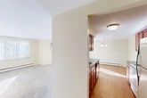Located at 8601 New Country Dr in Cicero, NY, this one-bedroom, one-bathroom residence offers a well-organized single-floor layout with a thoughtful mix of materials and finishes throughout. The living room is generously sized, featuring plush wall-to-wall carpeting, vertical blind-covered windows that allow abundant natural light, and baseboard heating. The space flows into a galley-style kitchen equipped with warm cherry wood cabinetry, granite countertops, a double sink, and white appliances including a range, microwave, and dishwasher. Hardwood flooring runs throughout the kitchen and dining area, which is accented by a classic chandelier overhead. The bedroom is a comfortable, well-proportioned retreat with soft carpeting, a window with vertical blinds, baseboard heating, and two sets of double closets providing ample storage. The bathroom is finished with tile flooring and tile wainscoting, a cherry wood vanity with a granite-topped countertop, a large mirror with overhead lighting, and an additional wall-mounted storage cabinet. Neutral wall tones and clean, bright finishes give the entire unit a light and welcoming ambiance throughout.