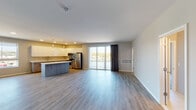 This contemporary single-floor unit offers a thoughtfully designed open-concept layout that seamlessly connects the living area and kitchen. The living space features light-toned luxury vinyl plank flooring that flows throughout, complemented by clean white walls and ample room for flexible furniture arrangements. Large sliding glass doors open to a private balcony, flooding the space with natural light and offering views of the surrounding neighborhood.

The kitchen is a standout feature, showcasing high-gloss white upper cabinetry paired with wood-toned lower cabinets, a light quartz countertop, and a full suite of stainless steel appliances including a refrigerator, range, microwave, and dishwasher. A central island provides additional prep and seating space. A secondary wet bar area with a sink and beverage cooler adds further functionality to the living zone.

The bedrooms are carpeted for comfort, each offering a calm, neutral palette and sliding glass door access to outdoor areas. The bathroom is finished with large-format tile in the walk-in shower, a mosaic tile floor, a quartz-topped vanity with wood cabinetry, and a well-placed mirror. Throughout the unit, the design emphasizes clean lines, modern finishes, and a cohesive, contemporary aesthetic.