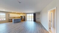 This contemporary single-floor unit offers a thoughtfully designed open-concept layout that seamlessly connects the living area and kitchen. The living space features light-toned luxury vinyl plank flooring that flows throughout, complemented by clean white walls and ample room for flexible furniture arrangements. Large sliding glass doors open to a private balcony, flooding the space with natural light and offering views of the surrounding neighborhood.

The kitchen is a standout feature, showcasing high-gloss white upper cabinetry paired with wood-toned lower cabinets, a light quartz countertop, and a full suite of stainless steel appliances including a refrigerator, range, microwave, and dishwasher. A central island provides additional prep and seating space. A secondary wet bar area with a sink and beverage cooler adds further functionality to the living zone.

The bedrooms are carpeted for comfort, each offering a calm, neutral palette and sliding glass door access to outdoor areas. The bathroom is finished with large-format tile in the walk-in shower, a mosaic tile floor, a quartz-topped vanity with wood cabinetry, and a well-placed mirror. Throughout the unit, the design emphasizes clean lines, modern finishes, and a cohesive, contemporary aesthetic.