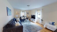 Located at 2 Garfield Street in Bay Shore, NY, this single-floor residence at Bayshore Manors R offers a comfortable and thoughtfully arranged living space with warm hardwood flooring flowing throughout. The living room serves as the heart of the home, featuring multiple windows that invite generous natural light and accommodate a generous seating arrangement. Warm cream-toned walls and classic flush-mount lighting contribute to the space's inviting ambiance. An adjacent dining area connects seamlessly to the kitchen via a pass-through window, providing an open and communicative layout. The kitchen is equipped with warm wood cabinetry, dark granite-style countertops, and stainless steel appliances including a gas range and built-in microwave, along with a window for added ventilation and natural light. A dedicated entryway area with a decorative mirror and console provides a welcoming transition into the home. The bathroom features classic white subway tile with a dark tile border, a pedestal-style vanity, and a full shower-tub combination. A separate utility area with cabinetry and a window offers practical storage and workspace. The bedroom is spacious and well-lit, completing this functional and comfortable single-floor layout.