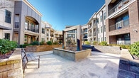 Located at 1106 Euclid Ave in Charlotte, NC's vibrant Dilworth neighborhood, this thoughtfully designed outdoor courtyard space serves as a central amenity within a multi-story residential community. The courtyard is defined by its sweeping, curved architectural layout, with the surrounding multi-story buildings—constructed with a blend of brick, stucco, and modern panel facades—enclosing the space to create a welcoming, semi-private atmosphere open to the sky above.

At the heart of the courtyard stands a striking sculptural water feature, set within a raised concrete basin and framed by geometric metalwork, serving as a compelling focal point for the paved gathering area. Wide, light-toned concrete pavers provide generous pedestrian pathways throughout, connecting distinct zones within the space. Raised stone planter beds add structured greenery, filled with seasonal flowers, shrubs, and ornamental trees that contribute color and texture throughout the year.

A spacious open lawn area provides a versatile, well-maintained green space ideal for recreation and relaxation. Benches and seating areas are thoughtfully placed along the pathways, inviting residents to linger. A pergola-shaded lounge area with outdoor furniture offers a comfortable retreat. The surrounding balconies and large windows of the residential buildings overlook the courtyard, enhancing the sense of community and connection throughout this well-appointed outdoor environment.