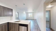 Located at 437 Beach and Ocean in Huntington Beach, CA, this modern apartment offers 880 square feet of thoughtfully designed living space across 2 bedrooms and 4 bathrooms on a single floor. The open-concept kitchen and living area serves as the heart of the unit, featuring light wood-style flooring, recessed lighting, and a central kitchen island with a white countertop and undermount sink. The kitchen is outfitted with dark wood cabinetry, stainless steel appliances including a French door refrigerator, gas range, and built-in microwave, complemented by a clean white tile backsplash. In-unit laundry is also conveniently accessible from the main living area. The primary bedroom spans 220 square feet and features large windows offering views of palm trees and the surrounding Huntington Beach streetscape. The second bedroom is carpeted and equally well-lit with dual windows. All four bathrooms are finished with white tile, modern vanities with dark countertops and wood cabinetry, and tub-shower combinations. The unit's neutral color palette, clean lines, and abundant natural light create a bright, contemporary coastal living environment.