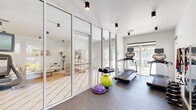 Located at 3200 N Haverhill Rd in West Palm Beach, Florida, this fitness center offers a bright, modern workout environment designed to support a comprehensive exercise routine. The space features a clean, contemporary aesthetic with crisp white walls, a durable dark-toned flooring surface, and sleek cylinder-style track lighting mounted to the ceiling throughout.

The cardio zone is equipped with multiple treadmills and elliptical machines, each fitted with individual display monitors for an engaging workout experience. A stationary bike adds further variety to the cardio offerings. For strength training, the space includes a dumbbell rack with a full range of free weights, resistance bands and cables mounted to the wall, and stability equipment such as exercise balls and a BOSU trainer.

Full-length wall mirrors line one side of the room, enhancing the sense of space while allowing users to monitor their form during exercise. Floor-to-ceiling glass panel walls and large windows flood the interior with abundant natural light and provide open views of the surrounding outdoor area, including what appears to be a pool deck. A glass-walled partition offers a visual connection to an adjacent lounge or community room. Safety features such as an emergency exit sign, a fire extinguisher, and an AED unit are also present, ensuring a secure workout environment.