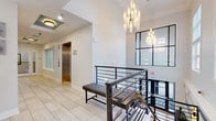 Located at 900 Crest Ln in Fort Lee, NJ, this thoughtfully designed amenity space combines contemporary aesthetics with functional comfort across a single well-appointed floor. The entry lobby immediately impresses with large-format light wood-toned tile flooring, soaring ceilings, and a striking cluster chandelier that cascades dramatic light throughout the space. A sleek staircase with dark metal railings and glass accents leads to adjacent areas, while elevator access adds convenience. A teal-accented coffered ceiling adds a bold architectural touch, complemented by a round pendant light and a decorative geometric wall panel that gives the main hall a refined, gallery-like feel. The lounge area is an inviting retreat, centered around a grand marble-surround fireplace with a mounted flat-screen display above. Coffered teal ceilings continue here, and plush seating arranged around a geometric wood coffee table creates a warm, social atmosphere. Double glass doors open directly to an outdoor pool area, filling the space with natural light and seamless indoor-outdoor connectivity. The kitchenette is outfitted with white shaker cabinetry, quartz countertops, a marble-veined backsplash, and stainless steel appliances, offering a polished and practical space for residents and guests alike.