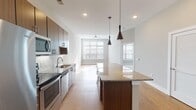 Located at 4429 NC-55 E in Cary, NC, this single-floor residence offers a thoughtfully designed open-concept layout that seamlessly connects the kitchen, dining, and living areas. The kitchen is a standout feature, showcasing rich dark-toned cabinetry, a full suite of stainless steel appliances including a French door refrigerator, range, and microwave, and a generous granite-topped island ideal for both meal prep and casual dining. Sleek pendant lighting with bold black fixtures adds a modern, contemporary flair above the island. Light wood-tone flooring runs throughout the main living areas, creating a warm and cohesive aesthetic. Large windows in the living area allow abundant natural light to fill the space, complemented by a ceiling fan for comfort. The bathroom continues the refined design with a dual-sink granite vanity, dark wood cabinetry with brushed metal hardware, and a large mirror that enhances the sense of space. The dollhouse view reveals a well-proportioned floor plan with dedicated bedroom areas and ample closet storage. Overall, the unit presents a clean, modern aesthetic with quality finishes throughout, making it a functional and stylish living space in the heart of Cary.