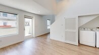 This contemporary two-floor space offers a thoughtfully designed layout that balances openness with functionality. The main living area is anchored by light hardwood flooring and crisp white walls, creating a bright and airy atmosphere. Large windows allow generous natural light to fill the space, while a glazed exterior door provides direct access to an outdoor area. A dramatic double-height ceiling opens the upper and lower levels visually, with a sleek pendant light fixture adding a refined modern touch to the vertical space.

The kitchen is well-appointed with dark wood cabinetry, light countertops, and a full suite of stainless steel appliances including a gas range, built-in microwave, refrigerator with ice maker, and dishwasher. A tile backsplash adds a clean, polished finish to the cooking area. Recessed lighting throughout ensures the space remains well-lit.

The bathrooms are finished to a modern standard, featuring tile flooring, a large vanity mirror, dark wood cabinetry with ample storage, and glass-enclosed tub-shower combinations. One bathroom is highlighted by a decorative mosaic tile accent within the shower surround, adding a subtle design element. Overall, the space presents a clean, contemporary aesthetic with quality finishes throughout.