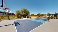 Located at 1812 W 4100 S in West Valley City, Utah, this well-appointed outdoor amenity area serves as a dynamic recreational hub designed for active community use. At its centerpiece are dual-purpose sport courts finished in a striking blue and gray surface, accommodating both pickleball and basketball, complete with nets and boundary markings. The courts are bordered by wide concrete walkways that provide easy access and transition seamlessly into the surrounding landscaped areas.

A dedicated outdoor grilling station with stainless steel BBQ equipment is conveniently positioned adjacent to the courts, accompanied by a vibrant red picnic table that offers a comfortable gathering space for socializing. Tall light poles are strategically placed throughout the area, ensuring the space remains fully functional during evening hours.

The grounds are thoughtfully landscaped with drought-tolerant ornamental grasses, native shrubs, gravel beds, and mature trees, reflecting a low-maintenance yet visually appealing design suited to the Utah climate. A lush lawn area is also visible, adding a soft green contrast to the hardscaped elements.

The backdrop features a modern multi-story residential building with bold red, blue, and white exterior accents, framed by sweeping views of the Wasatch mountain range under open blue skies, giving the entire space an inviting and energetic atmosphere.