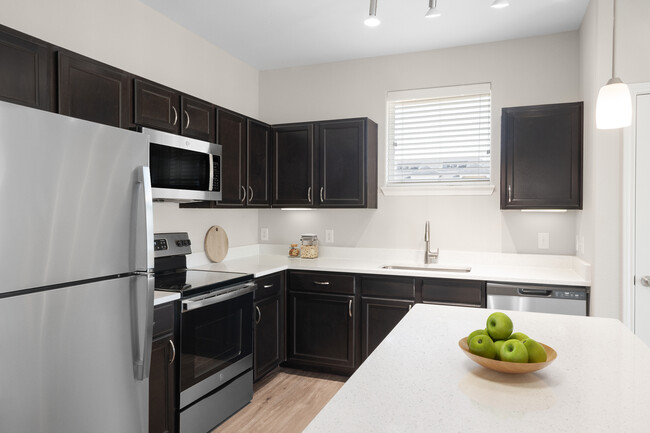 Kitchen with stainless steel appliances, quartz or granite countertop, espresso cabinetry, and hard surface vinyl plank flooring - Avalon at Pier 121