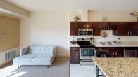 This single-floor residence offers a thoughtfully designed layout that balances comfort and functionality. The open-concept kitchen is a standout feature, showcasing rich dark-wood cabinetry, a granite-topped island, stainless steel appliances including a refrigerator, range, and built-in microwave, and light tile flooring that adds brightness throughout. The kitchen flows seamlessly into the living area, which is finished with soft carpeting and neutral walls, creating a cohesive and inviting atmosphere. The multiple bedrooms are generously sized, each featuring plush carpet, large windows fitted with horizontal blinds that allow for natural light control, and ample closet space with clean, modern double doors. Warm, neutral tones throughout give each bedroom a calm and restful character. The two bathrooms are well-appointed with light wood vanity cabinetry, white countertops, large mirrors, and light-toned tile flooring. One bathroom features a shower-tub combination, while the other is configured as a half bath. The overall design of the space is contemporary and understated, with consistent finishes and a neutral palette that provides a versatile backdrop for a variety of interior styles.