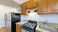 This single-floor unit is defined by its warm parquet wood flooring, which runs consistently through the living areas and bedrooms, lending a classic character to the interior. The layout, visible in the floor plan, reveals a well-organized arrangement of multiple rooms connected by a central corridor, offering a practical and functional flow throughout the space.

The kitchen is efficiently designed, featuring warm-toned wooden cabinetry that extends to the upper walls for ample storage. Granite countertops in a light, speckled finish provide durable workspace, complemented by a gas range with a stainless steel range hood above, a stainless steel refrigerator, and a window that brings in natural light. The flooring in the kitchen transitions to a light tile surface.

The bedrooms are bright and simply finished, with white walls and the same parquet flooring found throughout. Multiple windows fitted with blinds allow natural light to fill each room, offering views of the surrounding greenery. Closet doors are present in select rooms, providing practical storage.

The bathroom maintains a clean, all-white aesthetic with full tile surround walls, a soaking tub with chrome fixtures, a window for ventilation and light, and a white vanity with an integrated sink.