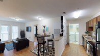 Located at 4017-4019 Wilshire Blvd in Wilmington, NC, this single-floor home offers a well-designed, open-concept layout that maximizes both functionality and comfort. The interior features warm hardwood flooring throughout, creating a cohesive and inviting atmosphere across the main living areas.

The kitchen is a central highlight, anchored by a peninsula with granite countertops that provides bar-height seating — ideal for casual dining or entertaining. A chalkboard accent column adds a charming, personalized touch near the kitchen, while the adjacent dining area accommodates a bistro-style high-top table and chairs, nestled atop a patterned area rug that defines the space.

The open flow connects seamlessly to the living room, where a wall-mounted flat-screen TV, a dark sofa, and natural light from nearby windows create a relaxed and welcoming environment. Decorative touches, including framed wall art and a mounted steer skull, lend the space a distinct personality.

A dedicated laundry area is conveniently accessible, equipped with a full-size washer and dryer, adding significant practical value. The home is well-lit with flush-mount ceiling fixtures throughout, and white walls provide a clean, bright backdrop that enhances the sense of openness. This single-story residence combines everyday convenience with a comfortable, lived-in aesthetic.