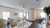 This single-story, 2-bedroom, 2-bathroom residence provides a thoughtfully designed layout that maximizes both comfort and functionality. The living area serves as the centerpiece of the home, featuring rich dark hardwood flooring that contrasts elegantly with the neutral, cream-toned walls. Crown molding adds a refined architectural detail, framing the space with a polished finish.

Natural light flows into the living room through multiple windows fitted with blinds, creating a bright and welcoming atmosphere. A ceiling fan with a classic brushed-gold fixture provides both practical ventilation and a subtle decorative accent. The generous proportions of the living area comfortably accommodate a full seating arrangement, as demonstrated by the neutral sofa set, accent chairs, and a glass-top coffee table centered over a patterned area rug.

The open flow of the space connects seamlessly to adjacent areas, contributing to an airy, cohesive feel throughout the home. The overall design aesthetic leans toward a clean, contemporary-neutral palette, making the space highly versatile and move-in ready for a variety of personal styles.
