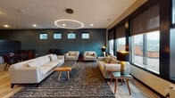 Located at 1001 Belknap Street in Superior, Wisconsin, this thoughtfully designed single-floor amenity space blends modern aesthetics with functional versatility. The open-concept layout connects several distinct areas, all unified by warm wood-look flooring and carefully curated design details.

The kitchen is a standout feature, showcasing a striking geometric-patterned accent wall in gold and black tones that creates a bold visual backdrop. A large waterfall-edge marble island with seating for multiple guests anchors the space, complemented by dark cabinetry, stainless steel appliances, a wall-mounted range hood, and pendant lighting that adds an industrial-chic flair.

The lounge area exudes a welcoming, upscale atmosphere with deep teal accent walls, a dramatic circular LED pendant light, and generous seating arrangements. Large windows with roller shades allow natural light to fill the room while framing views of the surrounding area, creating a bright and comfortable gathering space.

A casual dining area provides additional seating with round wooden tables, bistro-style chairs, a wall-mounted TV, and a slatted dark accent wall that adds texture and depth to the room.

The conference room offers a more formal setting, featuring a large wooden meeting table, leather executive chairs, a statement sputnik-style chandelier, and an eye-catching blueprint-themed wallpapered accent wall, making it ideal for professional gatherings or meetings.