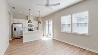 Located at 11100 Domain Dr in Jacksonville, FL, this thoughtfully designed one-bedroom, one-bathroom home offers a bright and modern living experience across a single floor. The open-concept layout seamlessly connects the living area and kitchen, creating an inviting and functional space bathed in natural light from multiple windows and a sliding glass door that opens to a private outdoor area.

The kitchen is a standout feature, equipped with stainless steel appliances including a French door refrigerator, electric range, and microwave. Crisp white shaker cabinetry reaches toward the ceiling, complemented by a subway tile backsplash and a generous island with a light quartz countertop and undermount sink — ideal for both meal prep and casual dining. Stylish pendant lights hang above the island, adding a contemporary touch. A ceiling fan anchors the open living space beneath vaulted ceilings.

The bedroom is well-proportioned, offering a ceiling fan, a walk-in closet, and large windows that frame outdoor views, filling the room with natural light. The bathroom features a walk-in glass shower, a vanity with a white countertop, and clean, neutral finishes throughout. Light wood-tone luxury vinyl plank flooring flows consistently across all rooms, tying the space together with a warm, cohesive aesthetic.