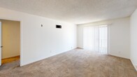 This single-story unit at 2925 Broadway, #117, in San Diego offers a straightforward, functional layout across several well-defined rooms. The entryway opens into a hallway with neutral white walls and textured ceilings, leading into a generously sized living area finished with wall-to-wall carpeting. Vertical blinds cover a sliding glass door, allowing natural light to filter into the space. An HVAC vent and thermostat are conveniently positioned along the wall.

The layout, as visible in the floor plan, includes a separate kitchen, multiple carpeted rooms, and two bathrooms. The kitchen is equipped with stainless steel appliances including a refrigerator, dishwasher, and electric range, complemented by white cabinetry, light countertops, hardwood-style flooring, and track lighting overhead. A peninsula provides additional prep or dining space.

The bedrooms are carpeted and feature windows with horizontal blinds that bring in natural light, along with HVAC vents for climate control. One bathroom includes a vanity with a single sink, a toilet, and a glass-enclosed shower, while the second bathroom features a full shower-tub combination with chrome fixtures. Both bathrooms have hardwood-style flooring, contributing to a clean, cohesive aesthetic throughout.