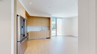 This contemporary single-floor unit showcases a clean, minimalist design throughout, with light hardwood flooring and crisp white walls creating a bright and cohesive aesthetic. The open-plan living and kitchen area serves as the heart of the space, where a well-appointed kitchen features flat-front light wood cabinetry, a marble-style quartz backsplash, white countertops, and stainless steel appliances including a built-in oven, gas cooktop, microwave, and refrigerator. A floor-to-ceiling sliding glass door connects the living area directly to an outdoor space, flooding the interior with natural light and providing open views of the surrounding cityscape. The bedrooms continue the modern theme, each offering light wood floors, clean white walls, and large sliding glass doors or windows that bring in ample daylight and outdoor views. One bedroom includes a built-in open closet system with frosted glass sliding doors, while another features open closet rods. The two bathrooms are finished with large-format neutral tiles, floating wood vanities, backlit mirrors, and frameless glass enclosures — one with a walk-in shower and the other with a full soaking tub and shower combination. The overall ambiance is refined, airy, and contemporary.