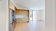 This contemporary single-floor unit showcases a clean, minimalist design throughout, with light hardwood flooring and crisp white walls creating a bright and cohesive aesthetic. The open-plan living and kitchen area serves as the heart of the space, where a well-appointed kitchen features flat-front light wood cabinetry, a marble-style quartz backsplash, white countertops, and stainless steel appliances including a built-in oven, gas cooktop, microwave, and refrigerator. A floor-to-ceiling sliding glass door connects the living area directly to an outdoor space, flooding the interior with natural light and providing open views of the surrounding cityscape. The bedrooms continue the modern theme, each offering light wood floors, clean white walls, and large sliding glass doors or windows that bring in ample daylight and outdoor views. One bedroom includes a built-in open closet system with frosted glass sliding doors, while another features open closet rods. The two bathrooms are finished with large-format neutral tiles, floating wood vanities, backlit mirrors, and frameless glass enclosures — one with a walk-in shower and the other with a full soaking tub and shower combination. The overall ambiance is refined, airy, and contemporary.