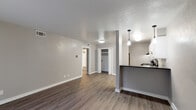 Located at 2712 Arroyo Ave in Dallas, TX 75219, this single-floor unit offers a clean, updated interior with a neutral color palette throughout. The open living area features durable wood-look plank flooring and connects seamlessly to the kitchen via a half-wall breakfast bar. The kitchen is equipped with white cabinetry, dark countertops, a black electric range, an under-cabinet range hood, and a single-basin sink — with a bifold-door closet providing convenient additional storage nearby. Pendant lighting over the kitchen bar adds a modern touch. The living room is bright and open, featuring a sliding glass door that allows natural light to flood the space and provides access to an outdoor area. The bedrooms are carpeted for comfort, with one room featuring a ceiling fan with light fixture and a window with outdoor views. The bathroom includes a full tub and shower combination with a curtain rod, toilet, and tile flooring, finished in a simple and functional style. Throughout the unit, consistent grey tones, white trim, and visible HVAC vents contribute to a cohesive and well-maintained aesthetic. The layout flows efficiently across all rooms, making practical use of the available space.