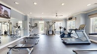 Located at 416 E North Pointe Dr in Salisbury, Maryland, this fitness center is a thoughtfully designed, single-floor facility offering a comprehensive workout environment. The space is finished with cool blue-gray walls, crisp white crown molding, and durable dark rubber flooring, creating a clean and functional aesthetic throughout.

The facility is generously sized, providing ample room for a wide range of exercise equipment. Cardio options include treadmills, an elliptical, a stationary recumbent bike, and a rowing machine, all arranged to allow comfortable spacing between users. A multi-functional cable machine serves as a centerpiece for strength training, complemented by a full rack of dumbbells and multiple adjustable benches for free weight and resistance exercises.

Full-length mirrors line one wall, enhancing the sense of space while allowing users to monitor their form. A wall-mounted flat-screen television adds convenience for those looking to stay entertained during workouts. The ceiling features a ceiling fan paired with recessed lighting, ensuring consistent air circulation and visibility throughout.

Multiple large windows along the perimeter flood the interior with natural light and offer views of the surrounding community. A glass-paneled door provides direct exterior access. The overall ambiance is bright, airy, and well-maintained, making this fitness center a practical and inviting space for daily exercise.