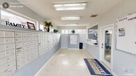 Located at Cliffdale Crossing Apartments in Fayetteville, NC, this dedicated mail room serves as a central hub for resident correspondence and package services. The space is designed with functionality and accessibility in mind, accommodating a large community with ease. Dominating the longest wall is an expansive, floor-to-ceiling bank of individual white mailboxes, providing secure mail storage for a significant number of residents. A second, smaller cluster of mailboxes is positioned on an interior dividing wall, ensuring efficient organization throughout the room. A wide service counter runs along one end of the space, offering a convenient area for residents to sort mail or interact with staff through the adjacent glazed office window. The room is finished with light-toned tile flooring that reflects the ample overhead fluorescent lighting, creating a bright and clean environment. Multiple windows along the exterior wall bring in natural light and offer views of the surrounding community. Touches of greenery from potted plants placed atop the mailbox units add a welcoming, community-oriented feel. A branded Cliffdale Crossing entryway mat greets visitors at the door, reinforcing the space's identity as a well-maintained community amenity.