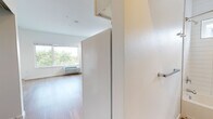 Located at 3244 Federal Blvd in Denver's 80211 corridor, this single-floor unit offers a clean, modern interior defined by light hardwood-style flooring and bright white walls throughout. The open kitchen is well-appointed with white cabinetry, a full suite of appliances including a refrigerator, electric range, microwave, and dishwasher, along with a sink and ample counter space. Recessed lighting enhances the kitchen's functionality, while an adjoining area provides flexibility for dining or additional living space.

The living area features natural light from generously sized windows, offering views of surrounding greenery and the broader Denver cityscape. A wall-mounted PTAC unit provides climate control. The bedroom includes warm hardwood-style flooring, a built-in closet for storage, a dedicated desk surface, and a window with an urban view. The bathroom is finished with crisp white horizontal tile surrounding a full soaking tub and shower combination, complemented by chrome fixtures, a grab bar, a small privacy window, and continuous hardwood-style flooring. The overall aesthetic is minimal, functional, and well-maintained.