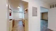 This single-floor residence offers a well-organized layout that balances functional living spaces with comfortable design. The galley-style kitchen is outfitted with warm wood cabinetry, granite-look countertops, a double-basin stainless steel sink, and white appliances including an electric range, dishwasher, and refrigerator. Ample upper and lower cabinet storage lines both sides of the kitchen, maximizing utility in the space.

The living area is a standout feature, highlighted by a full brick accent wall with a wood-burning fireplace that serves as a natural focal point. A sliding glass door with vertical blinds allows natural light to filter in while providing outdoor access. The hardwood-style flooring throughout the main living areas adds warmth and continuity to the space.

Two bathrooms serve the residence. One features a full bathtub and vanity with ample counter space, while the second offers a walk-in shower with mosaic tile flooring and clean white tile surround, accented by chrome fixtures and grab bars. Both bathrooms continue the hardwood-style flooring found throughout the home.

A carpeted bedroom provides a soft, quiet retreat, and an electrical panel is conveniently accessible in the hallway. The overall aesthetic is clean and neutral, offering a versatile canvas for personalization.