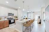Located at 9295 Ashland Ave in Pensacola, Florida, this single-story residence offers a well-designed, contemporary living environment with a bright and cohesive aesthetic throughout. The open-concept kitchen serves as a central hub, featuring a large island with a stainless steel sink, pendant lighting, warm wood cabinetry paired with crisp white upper cabinets, quartz countertops, and stainless steel appliances including a refrigerator and dishwasher. The kitchen flows seamlessly into the living area, which is bathed in natural light from oversized windows with blinds and access to an outdoor area. Ceiling fans are present throughout the home, enhancing comfort in each room. The living space is generous and versatile, accommodating both a lounge and a separate seating or home office area. The bedrooms are well-proportioned, each featuring large windows, ceiling fans, and light wood-style flooring. The bathrooms are outfitted with warm wood vanities, white quartz countertops, large mirrors, and direct access to spacious walk-in closets equipped with wire shelving systems. A dedicated flex room provides an ideal space for a home office or secondary sitting area. Throughout, neutral tones, light flooring, and consistent finishes create a clean, modern, and welcoming atmosphere.