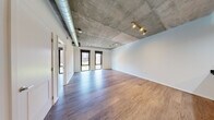 Located at 1025 N Fillmore St in Arlington, Virginia, this single-floor residence offers a compelling blend of industrial design and modern finishes. The open-concept living area immediately impresses with its exposed concrete ceiling, visible ductwork, and track lighting, creating a distinctly urban loft aesthetic. Large black-framed windows flood the space with natural light and provide views of the surrounding cityscape.

The kitchen is well-appointed with light wood cabinetry, dark granite countertops, a subway tile backsplash, and a full suite of stainless steel appliances including a refrigerator, range, and microwave. A peninsula with a generous granite countertop connects the kitchen seamlessly to the living area, making it ideal for both cooking and entertaining.

The bedroom features its own black-framed window with outdoor access, a ceiling fan mounted to the exposed concrete ceiling, and ample space for furnishings. Additional rooms offer the same consistent hardwood-style flooring and clean white walls throughout.

The bathroom stands out with elegant marble-style tile covering the walls and surrounding a soaking tub and a separate glass-enclosed shower. A wood vanity with a dark granite countertop and a large mirror completes this refined space. Overall, the residence delivers an industrial-modern ambiance with high-quality finishes throughout.