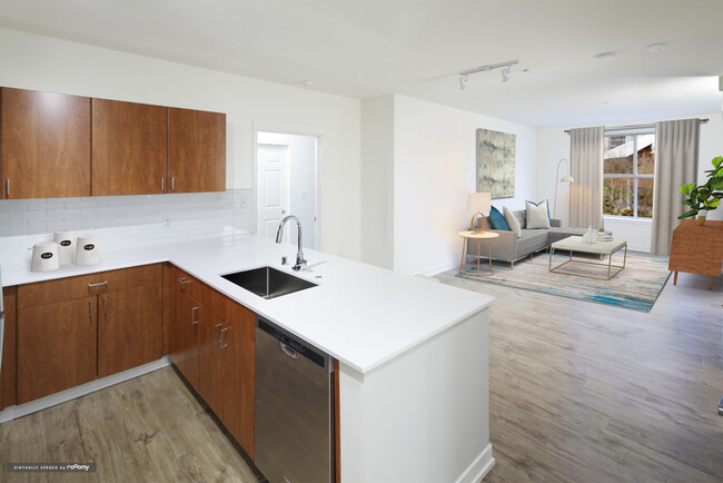 Renovated Package I kitchen and living area with white quartz countertops, oak cabinetry, stainless steel appliances, tile backsplash, and hard surface flooring - Avalon Bellevue