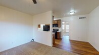 This single-floor residence offers a functional and comfortable layout with a clean, neutral aesthetic throughout. The living area is generously sized, finished with plush carpeting and equipped with a ceiling fan. Large windows and a front entry door allow natural light to fill the space, creating a bright and welcoming atmosphere.

The kitchen is thoughtfully designed and partially open to the living area via a pass-through window, maintaining a connected feel while defining each space. Rich warm-toned wood cabinetry pairs with marble-style countertops, and the kitchen is fully equipped with black appliances including a refrigerator, electric range, and over-the-range microwave. The kitchen floor features hardwood-style flooring that extends into the adjoining entry and hallway areas, providing a smooth transition between spaces.

The bathroom continues the warm design language with matching wood cabinetry, a marble-style countertop, a single undermount sink, and a large framed mirror above. Hardwood-style flooring carries through here as well, and a walk-in closet or storage area is accessible directly from the bathroom.

Overall, the space presents a cohesive and practical design with consistent finishes, comfortable flooring choices, and a layout that maximizes usability across the main living, kitchen, and bathroom areas.