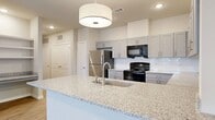 This well-appointed 4-bedroom, 2-bathroom single-floor residence offers a thoughtfully designed layout with modern finishes throughout. The kitchen serves as a central highlight, featuring gray shaker-style cabinetry, granite countertops, a subway tile backsplash, and a full suite of appliances including a stainless steel refrigerator, electric range, microwave, and dishwasher. A large peninsula with a pendant light overhead provides additional workspace and a casual dining option. Adjacent to the kitchen, a built-in shelving nook with a granite ledge offers a practical workspace or display area. The living room is bright and open, with light wood-style flooring, recessed lighting, and a door leading to an outdoor area. The four bedrooms feature plush carpeting and closets with built-in shelving, offering ample storage. Two full bathrooms are finished with gray vanity cabinetry, granite countertops, and light wood-style flooring. One bathroom features a double-sink vanity, while the other benefits from a window that brings in natural light. A connecting hallway ties the layout together efficiently, creating a cohesive and functional living environment throughout.