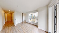 Located at 3075 Devonshire Ave in Halifax, NS, this thoughtfully designed unit offers a clean, contemporary aesthetic throughout its well-utilized single floor. Light-toned wood-look flooring runs continuously through the living spaces, complementing the crisp white walls and creating a bright, cohesive atmosphere.

The open-concept living area is anchored by a large picture window that frames views of the surrounding neighbourhood and mature trees, filling the space with natural light. An adjoining kitchen features a generous white quartz island with an undermount sink, stainless steel appliances including a range, over-the-range microwave, and refrigerator, plus a combination of white and warm wood-toned upper cabinetry with under-cabinet lighting.

The bedroom is a quiet, neutral-toned room with its own large window, light wood flooring, and clean-lined finishes. Two full bathrooms serve the unit: one features a full soaker tub with white subway tile surround and a floating vanity, while the second includes a sliding-glass enclosed walk-in shower with matching tile, offering added convenience and flexibility.

Two hallways connect the spaces efficiently, contributing to a practical and functional layout. The overall ambiance is modern, clean, and move-in ready.