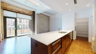 Located at 725 Johnson Ct in Cleveland's vibrant Ohio City neighborhood, this single-floor unit masterfully blends industrial character with contemporary design. Exposed brick walls and structural steel columns serve as defining architectural elements throughout, paying homage to the building's industrial origins while complementing clean, modern finishes.

The open-concept living and kitchen area is a standout feature, anchored by a large island with a sleek white countertop and dark cabinetry. Stainless steel appliances, a stainless range hood, white upper cabinetry with tile backsplash, and recessed lighting complete the well-appointed kitchen. Warm hardwood-style flooring flows through the living areas, which benefit from generous natural light through large floor-to-ceiling windows and sliding glass doors that open to an outdoor space.

The bedrooms offer soft carpeting, recessed cove lighting, and continued exposure to the building's original brick. Ample closet space, including a walk-in closet, adds practical functionality. Two bathrooms are finished with light wood-toned tile, one featuring a soaking tub and shower combination, and the other a glass-enclosed walk-in shower with a wall-mounted vanity and glass shelving. The overall ambiance is sophisticated yet approachable, making this a distinctive urban retreat.