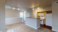 Located at 8603 N Loop 1604 W Access Rd in San Antonio, TX, this single-floor unit offers a well-organized layout designed for comfortable, everyday living. The open-concept living and dining area is finished with plush carpeting and neutral-toned walls, creating a warm and inviting atmosphere. Track lighting overhead provides consistent illumination throughout the shared space.

The kitchen is defined by a wraparound peninsula that separates it from the living area, offering both counter space and a natural division between rooms. Warm honey-toned wood cabinetry lines the walls, complemented by a full suite of white appliances including a range, over-the-range microwave, and refrigerator. A decorative wine rack built into the upper cabinetry adds a distinctive touch, while dark hardwood flooring grounds the kitchen area.

The bedrooms are carpeted and bright, each benefiting from natural light through blinded windows. One bedroom features a ceiling fan, while the primary bedroom includes access to a walk-in closet. The bathroom is cleanly appointed with white tile surrounding a full soaking tub and shower combination, set against hardwood-style flooring.

The entryway is welcoming, with multiple windows flanking the front door and allowing ample natural light into the space.