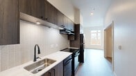 Located at 420 Center St NE in Salem, Oregon, this one-bedroom, one-bathroom unit offers a thoughtfully designed layout that maximizes every square foot. The galley-style kitchen is a standout feature, showcasing dark espresso cabinetry with under-cabinet lighting, a white quartz countertop, a stainless steel sink with a matte black faucet, and a textured tile backsplash. Black appliances — including a range, dishwasher, and refrigerator — complete the modern aesthetic. Wood-style luxury vinyl plank flooring flows throughout the space, lending warmth and continuity. The open living area benefits from a large window that draws in natural light and frames views of the surrounding greenery. The bedroom is a comfortable, quiet retreat with its own generous window overlooking mature trees, offering a serene outdoor connection. The bathroom features a full soaking tub with a matte black handheld shower system, grab bars for accessibility, and consistent modern finishes. Clean white walls and recessed lighting throughout the unit create a bright, airy ambiance. The overall design balances contemporary style with functional efficiency, making this a well-appointed urban residence in the heart of Salem.