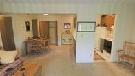 This single-floor residence offers a practical and welcoming layout designed for comfortable everyday living. The kitchen is efficiently appointed with full-size appliances, including a refrigerator and dishwasher, and features tile flooring that transitions seamlessly into the adjacent living and dining areas. A half-wall partition defines the kitchen space while maintaining an open, connected feel throughout the main living area.

The dining area is carpeted and comfortably accommodates a full dining set, with warm wood tones from the table and chairs adding a classic, homey character to the space. A charming country-style accent cabinet with decorative rooster motifs serves as a focal point in the room, complementing the overall warm aesthetic.

Neutral wall colors and soft, ambient lighting keep the interior feeling bright and inviting. A closet with folding doors is visible from the dining area, offering convenient storage. Decorative framed artwork adds personal touches to the walls, reinforcing the cozy, lived-in ambiance. The consistent use of warm tones, carpet, and country-inspired accents throughout creates a cohesive and comfortable environment well-suited for relaxed, day-to-day living.