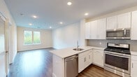 Located at 41 W Prospect St in Waldwick, NJ, this thoughtfully designed one-bedroom, one-bathroom unit offers a clean, modern aesthetic throughout its single-floor layout. Warm hardwood-style flooring flows seamlessly across the entire space, creating a cohesive and inviting atmosphere.

The open-plan kitchen and living area serves as the heart of the unit. The kitchen is well-appointed with crisp white shaker cabinetry, light gray subway tile backsplash, quartz countertops, and a full suite of stainless steel appliances including a gas range, microwave, and a full-size refrigerator. A kitchen island provides additional counter space and casual seating.

The bedroom is generously sized, bathed in natural light through large windows that offer pleasant green views of the surrounding landscape. Recessed lighting enhances the bright, airy feel of the room. A dedicated walk-in closet features multi-level wire shelving, offering practical and well-organized storage.

The bathroom features neutral marble-look tile flooring, clean white walls, and a minimalist design that complements the overall aesthetic of the unit. Throughout the space, white panel doors, recessed lighting, and clean trim details contribute to a fresh, modern finish that is both functional and visually appealing.